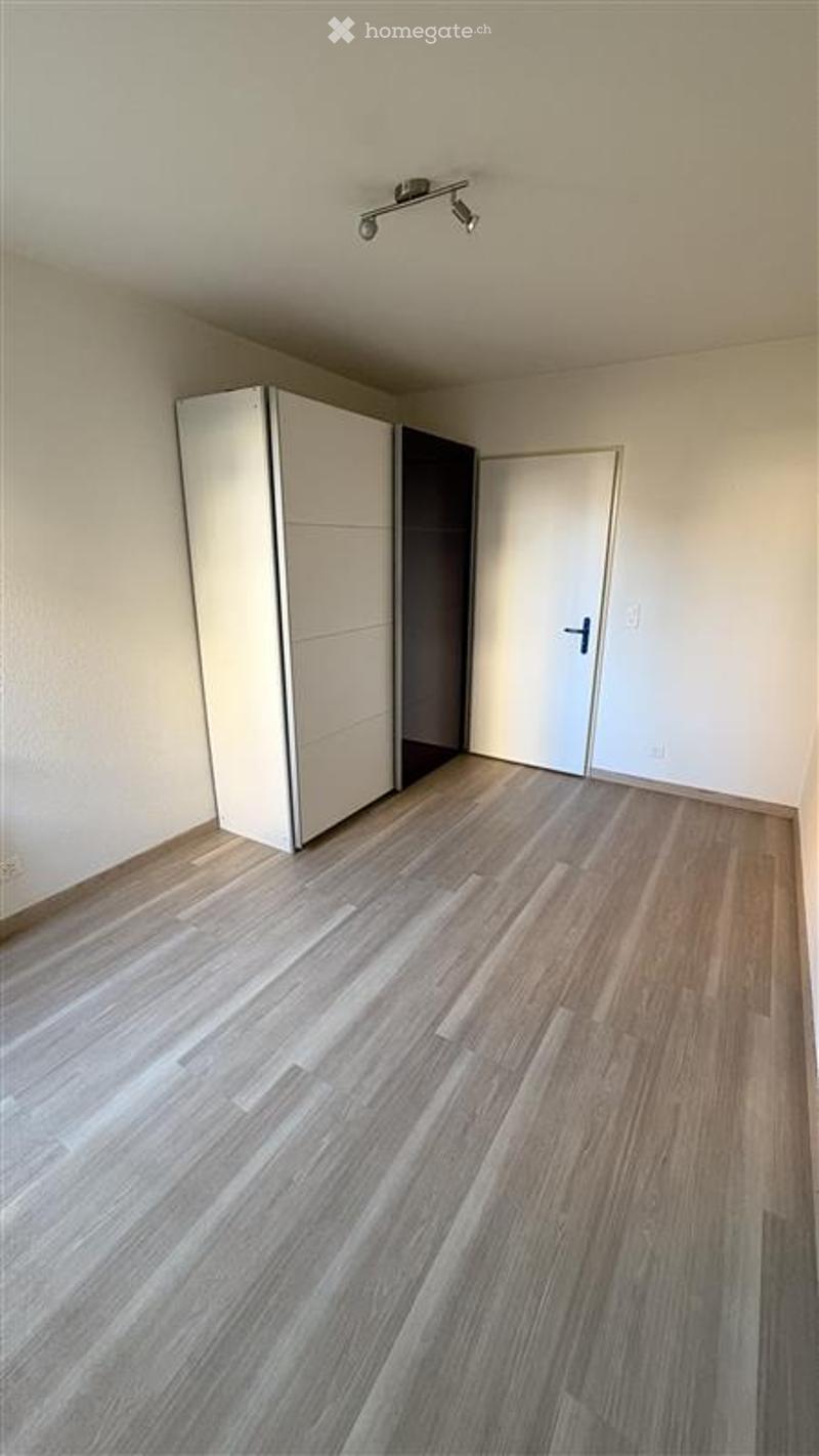 Empty room with light wooden flooring, white walls, a built-in wardrobe, and a closed door.