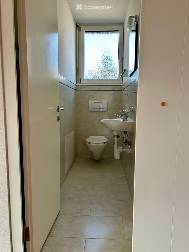 Modern bathroom with beige tiles, a toilet, a sink with a modern faucet, a mirror, and a frosted window above the sink.