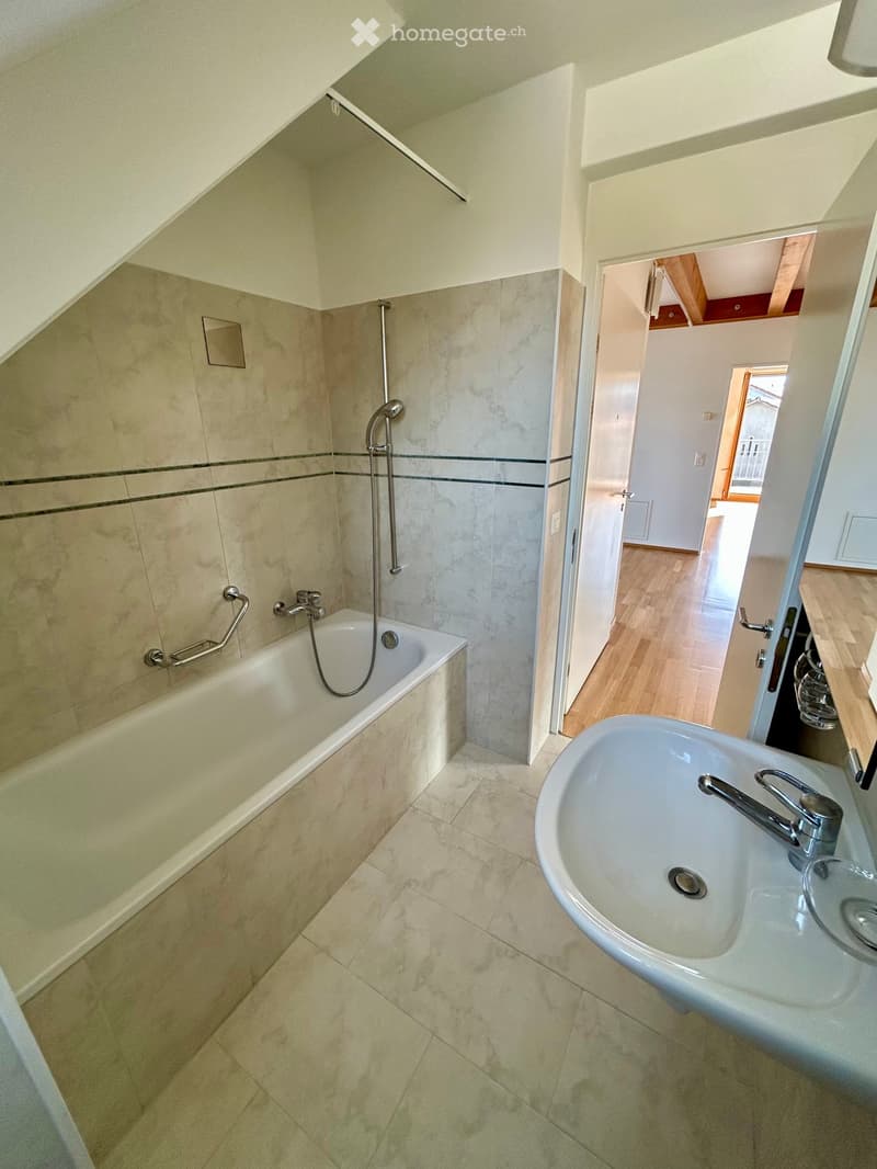 Bathroom with a bathtub, sink, and showerhead. The room features tiled walls and a wooden floor visible through an open doorway.