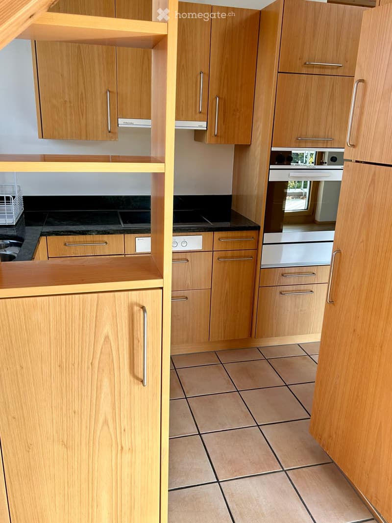 Modern kitchen with light wooden cabinets, stainless steel oven, and tiled floor.