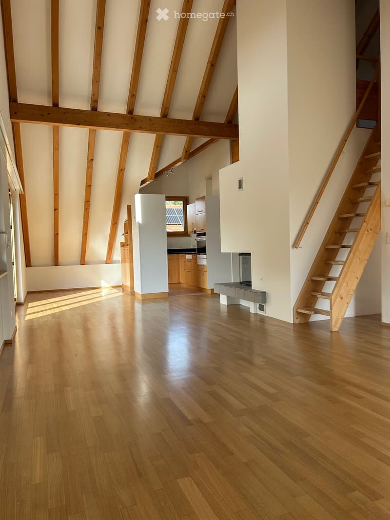 Open-plan space with wooden flooring, exposed wooden beams, a staircase leading to an upper level, and a small kitchen area with cabinets and appliances.