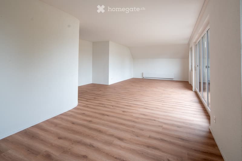 Empty room with wooden flooring, white walls, and large windows with glass doors leading to a balcony.