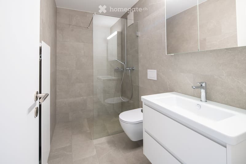 Modern bathroom with beige tiles, a white sink, toilet, and a glass-enclosed shower area.