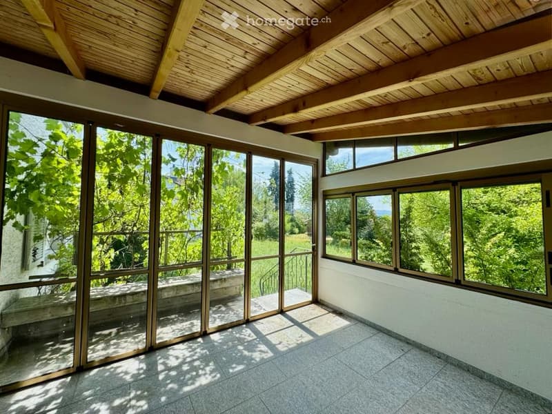 Bright, open room with large glass sliding doors leading to an outdoor area, wooden ceiling beams, and tiled floor.
