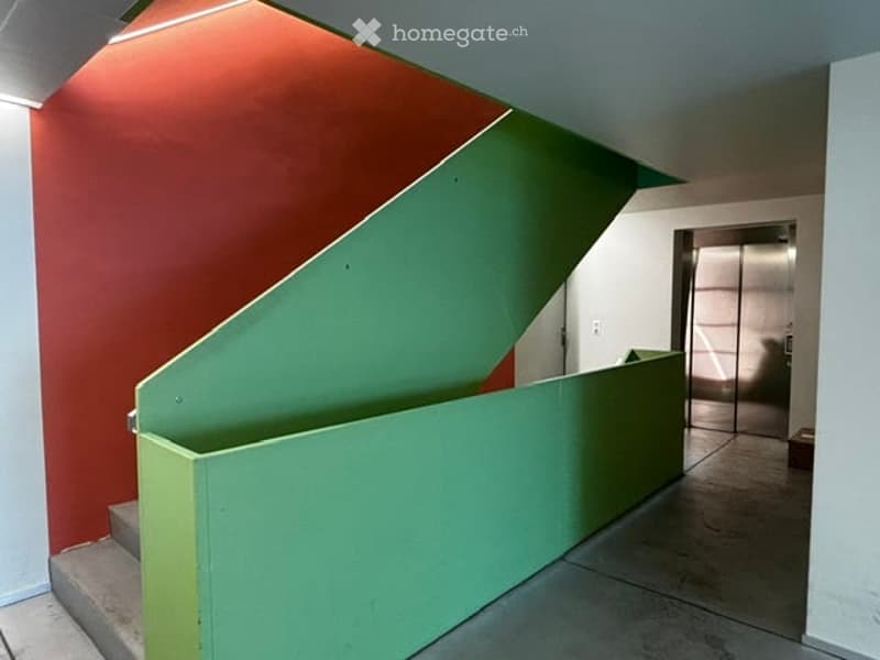 Modern hallway with a green staircase railing, red and white walls, and a sleek elevator in the background.
