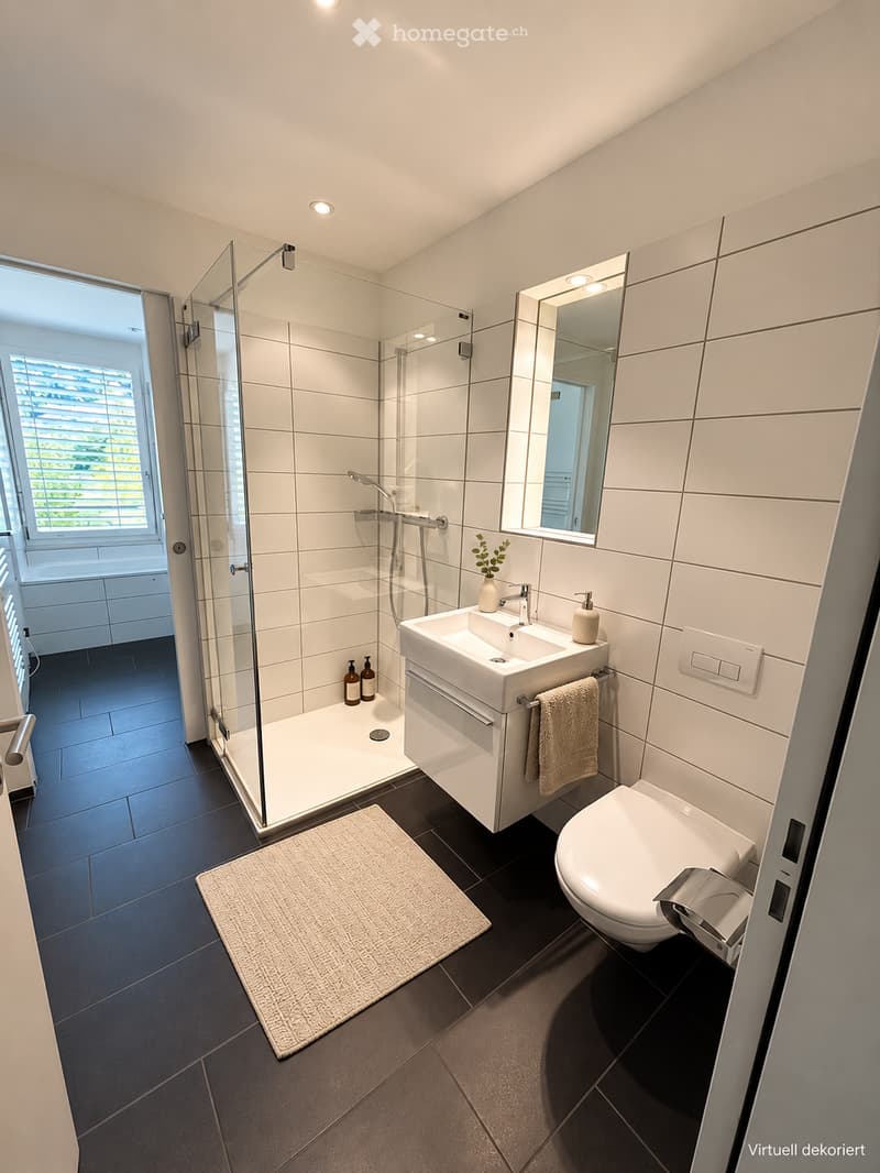 Modern bathroom with white tiles, a glass-enclosed shower, a white sink with a mirror, a toilet, and a small plant on the sink counter.