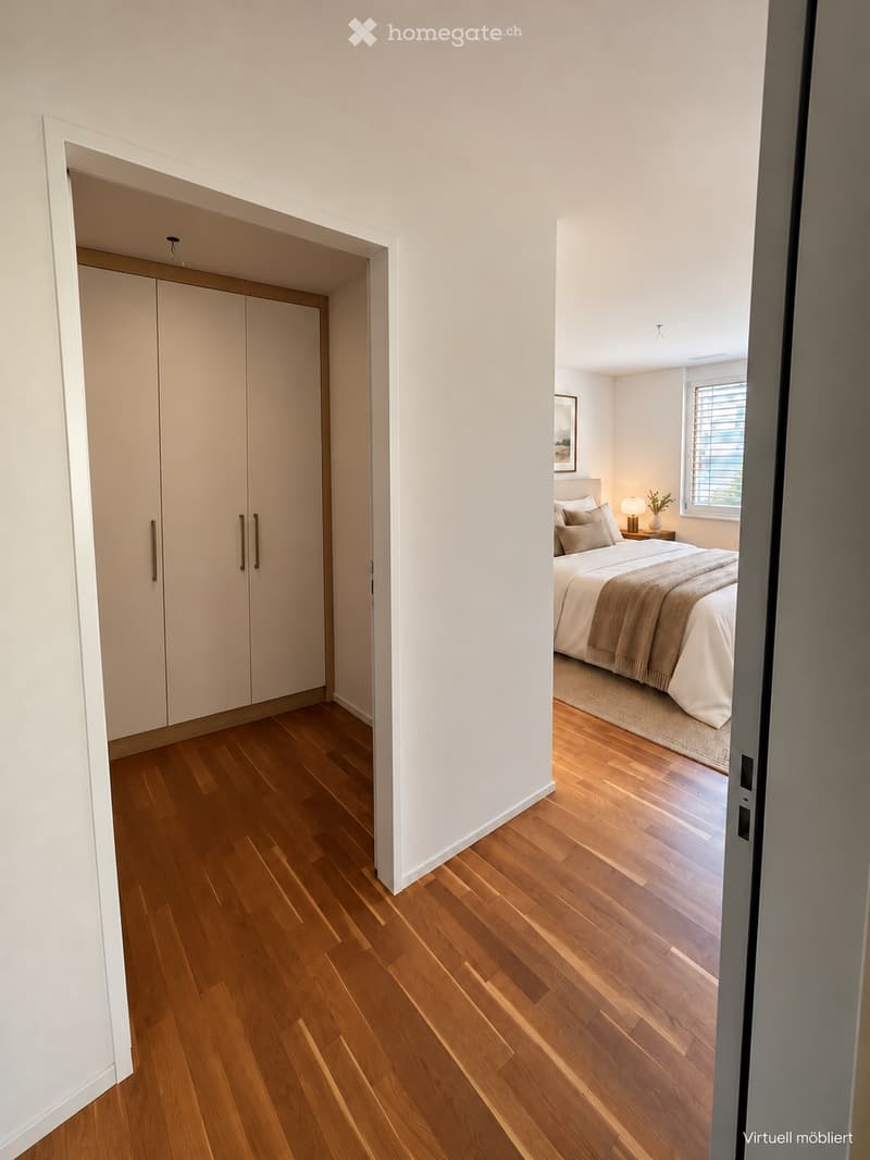 Spacious bedroom with wooden flooring, large wardrobe, neatly made bed with pillows and blankets, nightstand with lamp, and a small rug.
