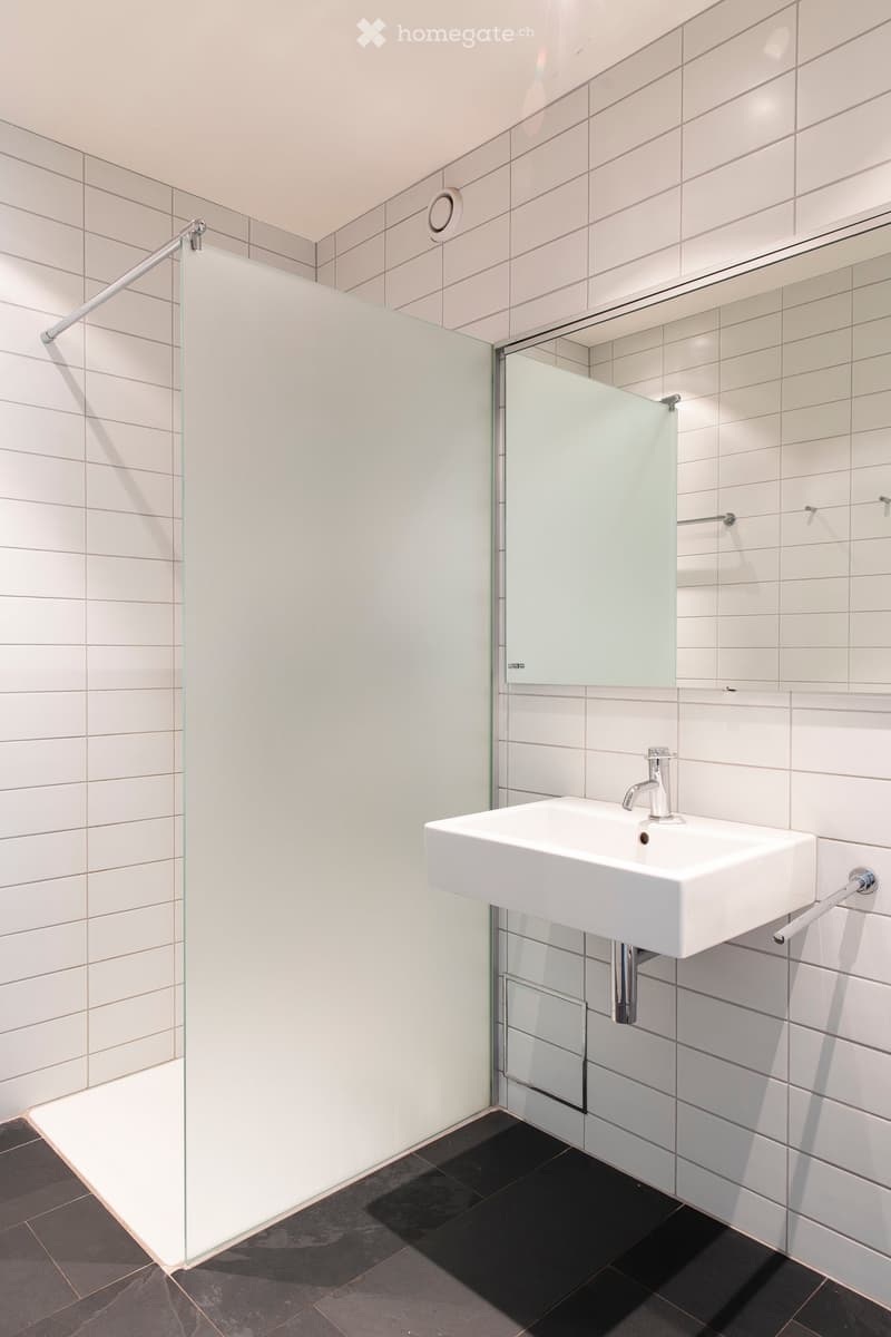 Modern bathroom with white tiles, a wall-mounted sink, a chrome faucet, a glass shower enclosure, and a built-in mirrored cabinet.
