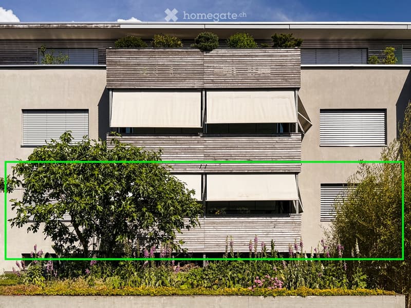 Modern two-story building with large windows, wooden shutters, and a rooftop garden with greenery and shrubs.