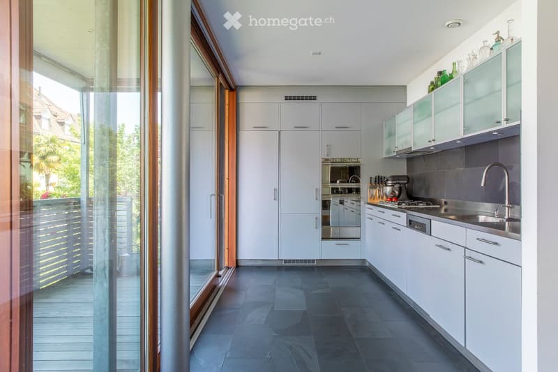 Modern kitchen with white cabinets, stainless steel appliances, and a large window overlooking a balcony. The kitchen features a sink with a modern faucet, an oven, a stove, and various kitchen utensils.