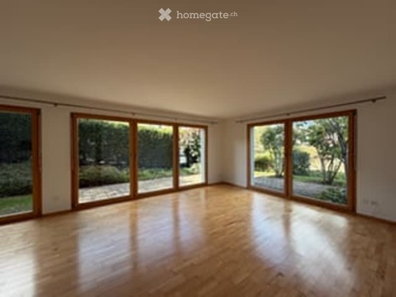 Bright, unfurnished room with large wooden-framed windows, wooden flooring, and white walls. The space is empty, showcasing natural light and an open layout.