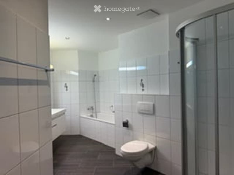 Modern bathroom with white tiled walls, dark brown tiled floor, bathtub, toilet, shower, and sink.