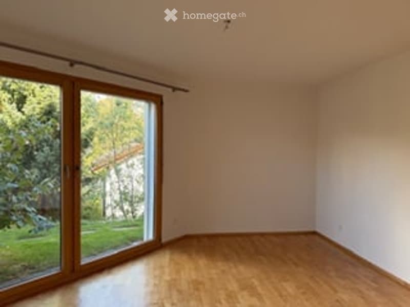 Empty room with wooden flooring, large window with wooden frame, and white walls.