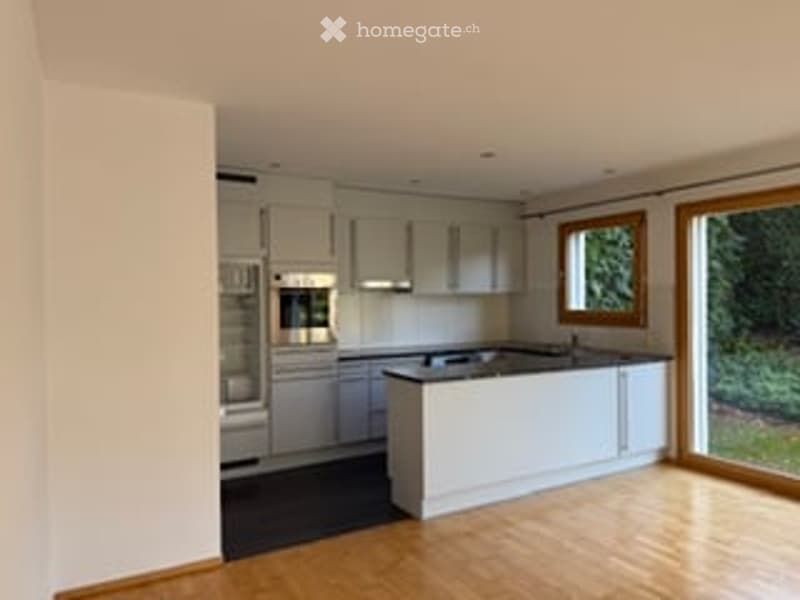 Modern kitchen with light grey cabinets, white island, and wooden flooring.