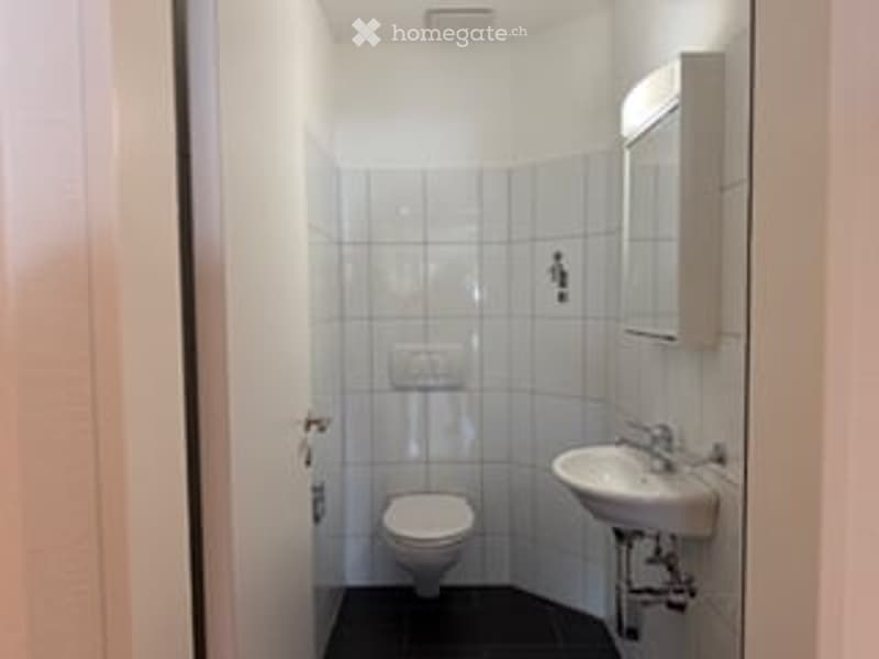 Small, clean bathroom with white tiled walls, a toilet, a sink with a mirror, and a faucet.