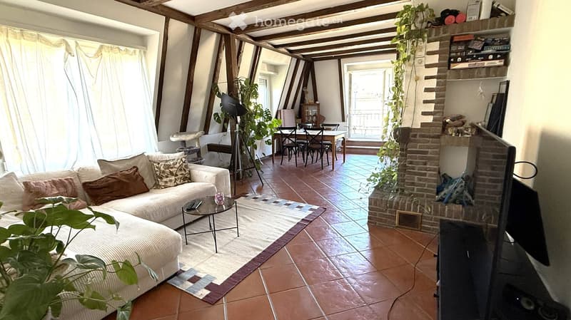Living room with exposed wooden beams, tiled floor, fireplace, sofa, coffee table, TV, dining area with table and chairs, and cat tree.