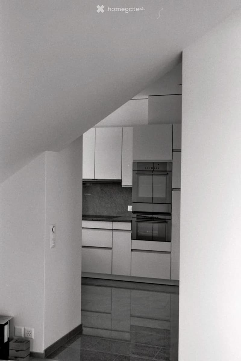 Modern kitchen with sleek, grey cabinets, a built-in oven, and a dark tiled floor.