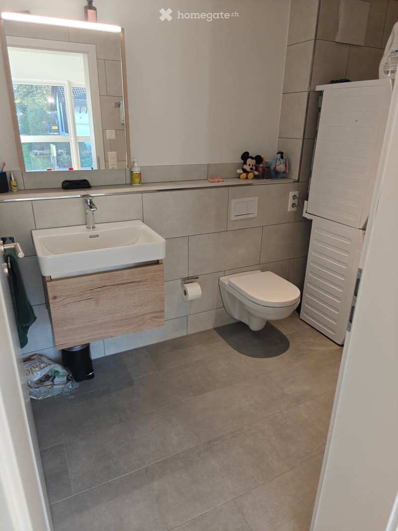 Modern bathroom with a white sink, toilet, large mirror, wooden cabinet, and tiled floor.