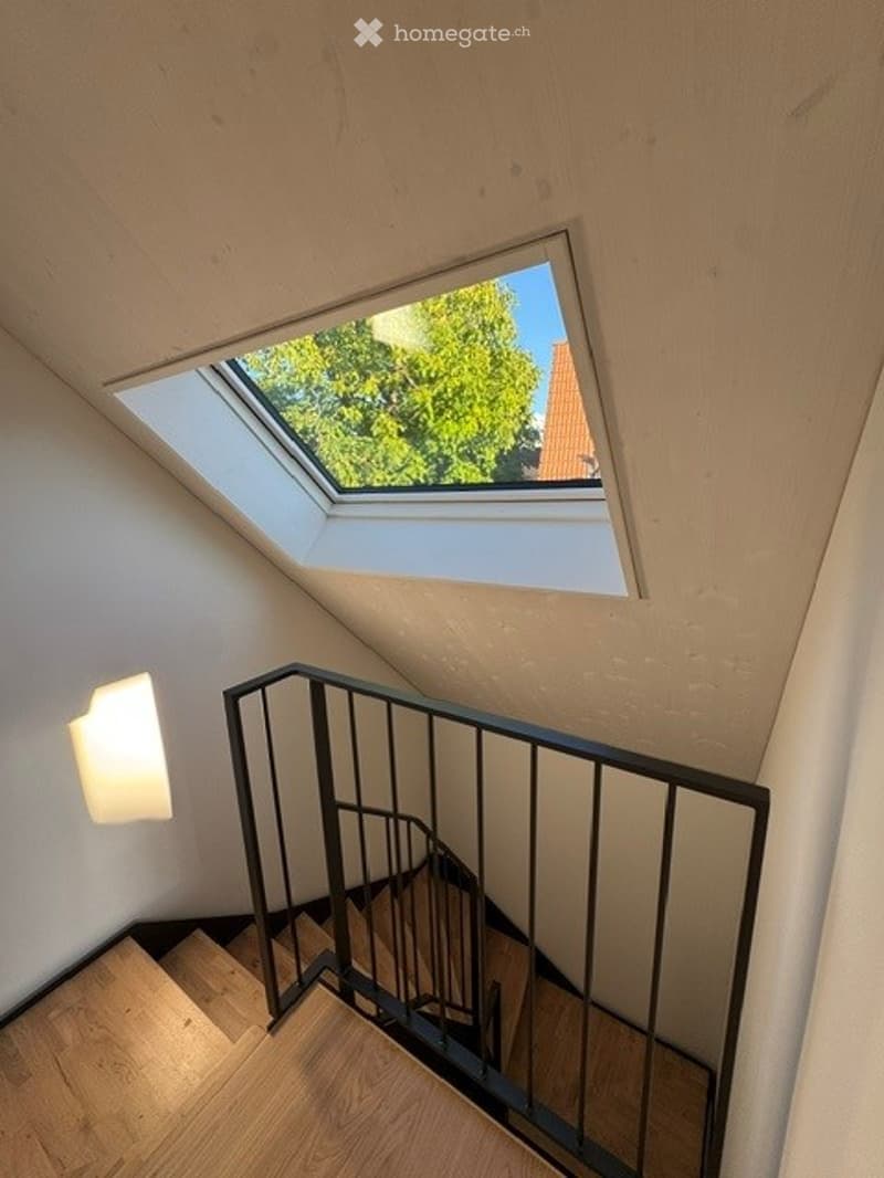 Staircase with wooden steps, black metal railing, and a skylight window at the top, allowing natural light into the space.