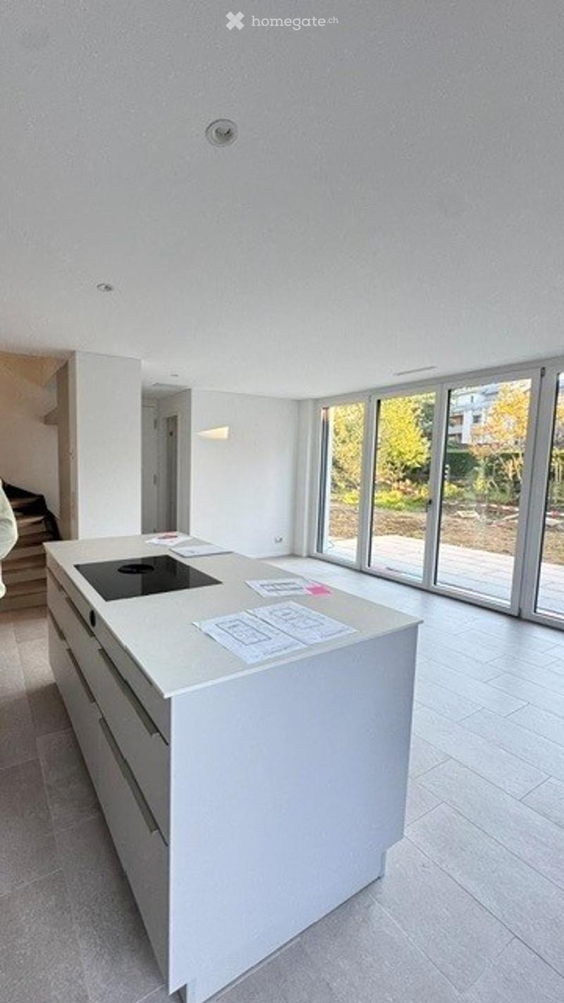 Modern kitchen with a white island, induction cooktop, and large windows offering a view of the garden.