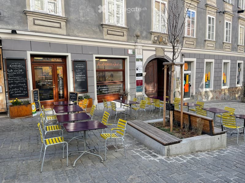 Outdoor seating area with tables and chairs in front of a building with a sign reading "Koch Genuss Atelier".