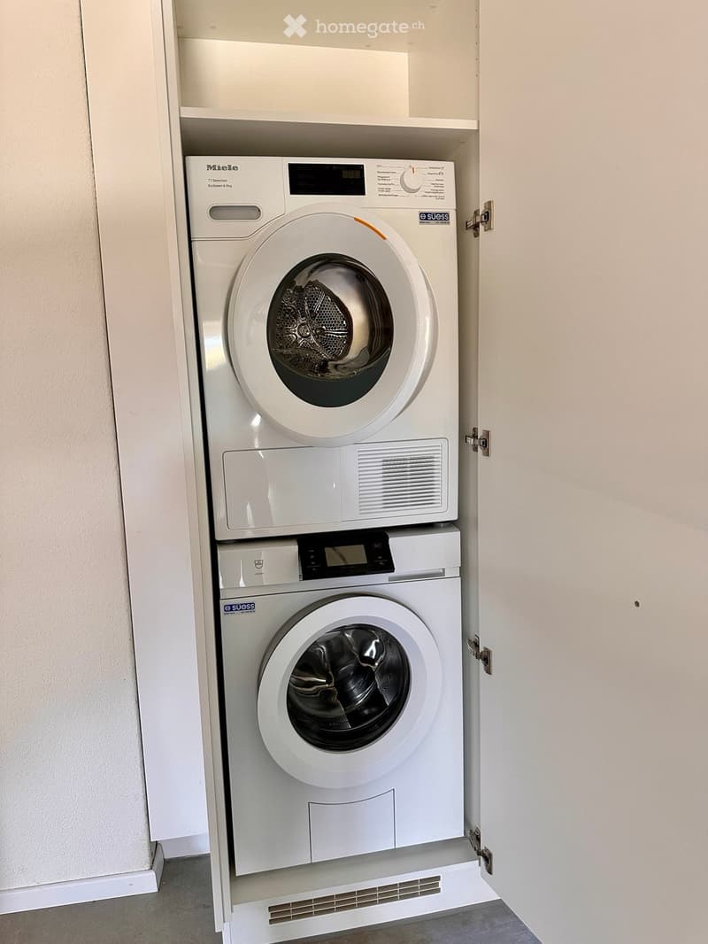 Compact, built-in laundry area with a washing machine and dryer stacked vertically inside a cabinet.