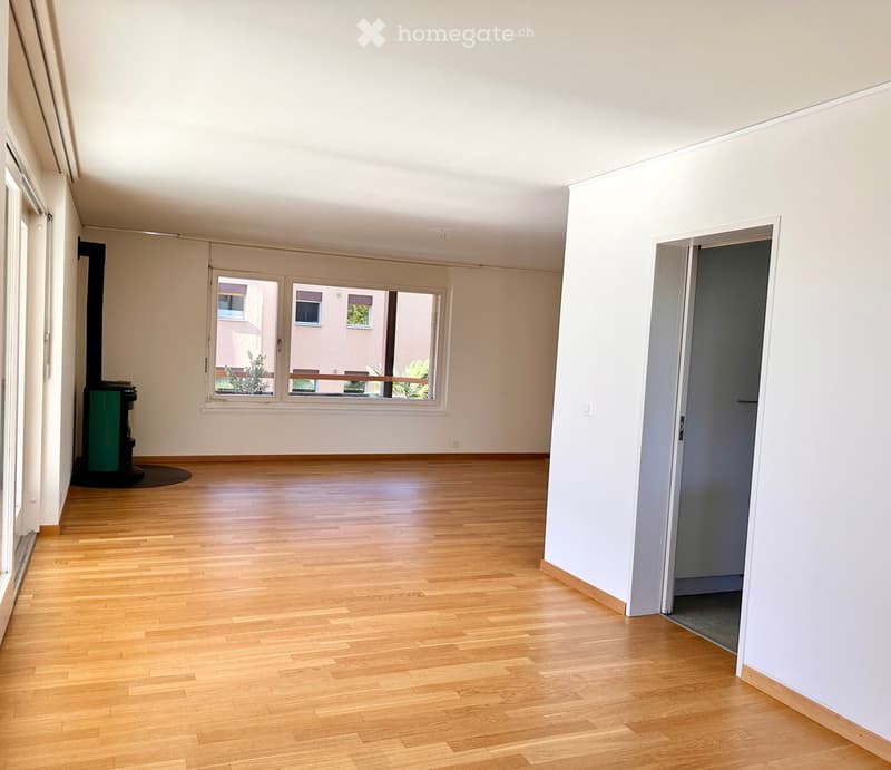 Empty room with wooden flooring, white walls, large windows, and a fireplace in the corner.