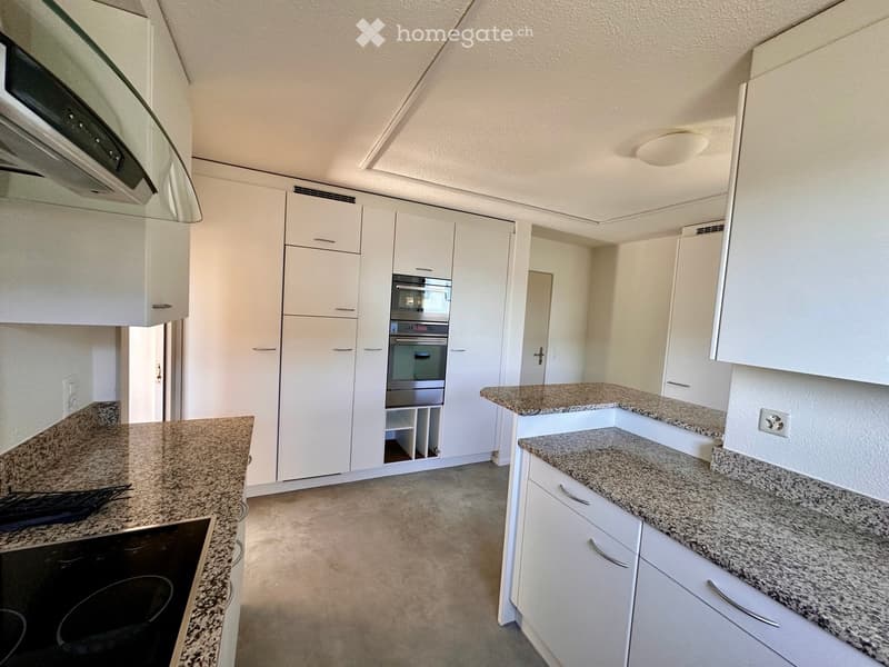 Modern kitchen with white cabinets, granite countertops, built-in oven, and range hood.