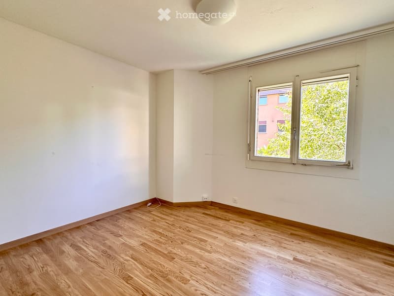 Empty room with light-colored walls, wooden flooring, and large windows with blinds. No furniture or equipment is present.