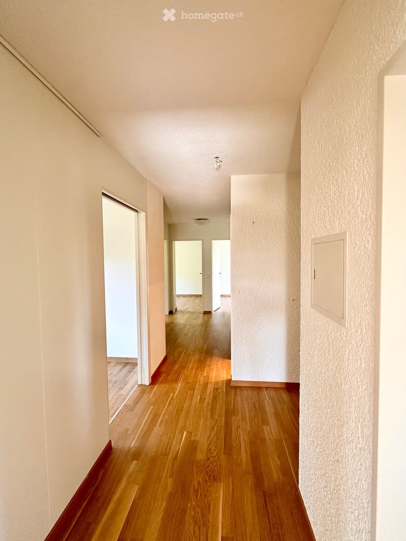 A narrow hallway with wooden flooring, white walls, and several doors leading to other rooms.