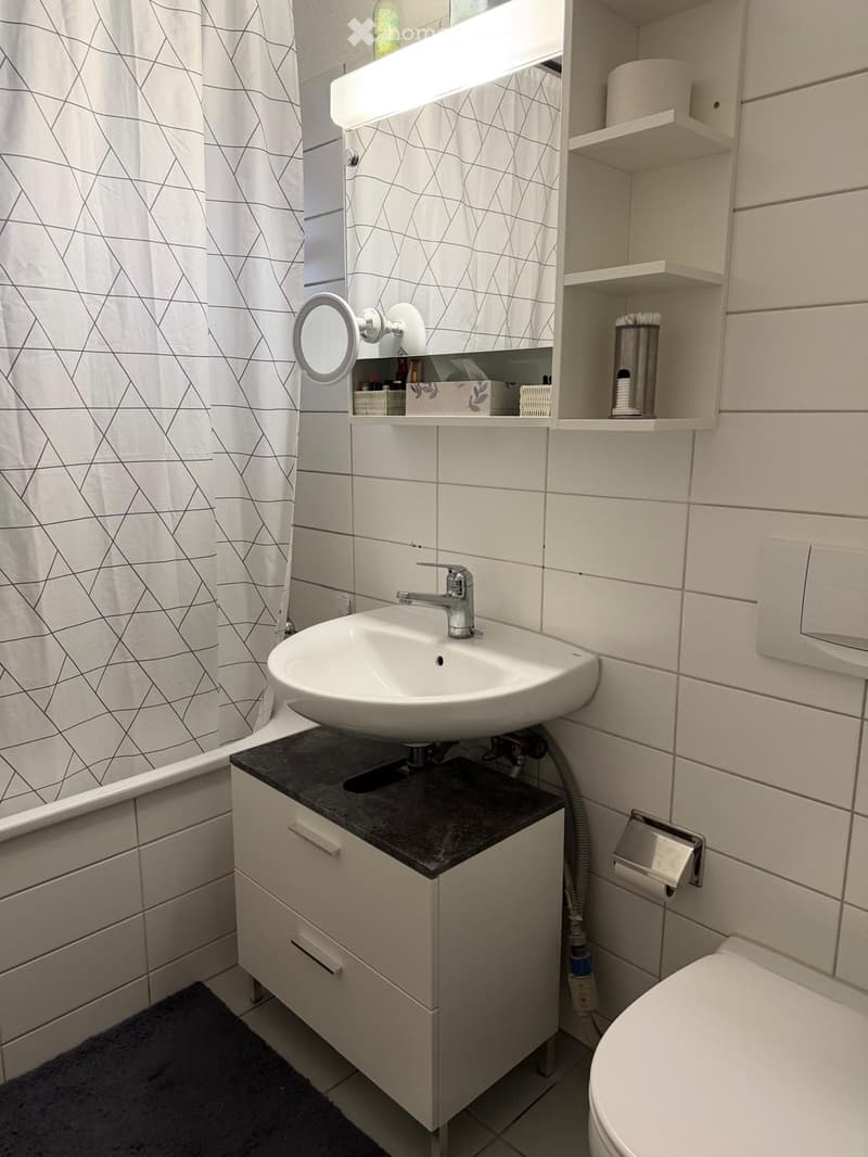 Modern bathroom with white tiles, a floating sink with a black countertop, a built-in cabinet, a toilet, and a shower curtain with a geometric pattern.