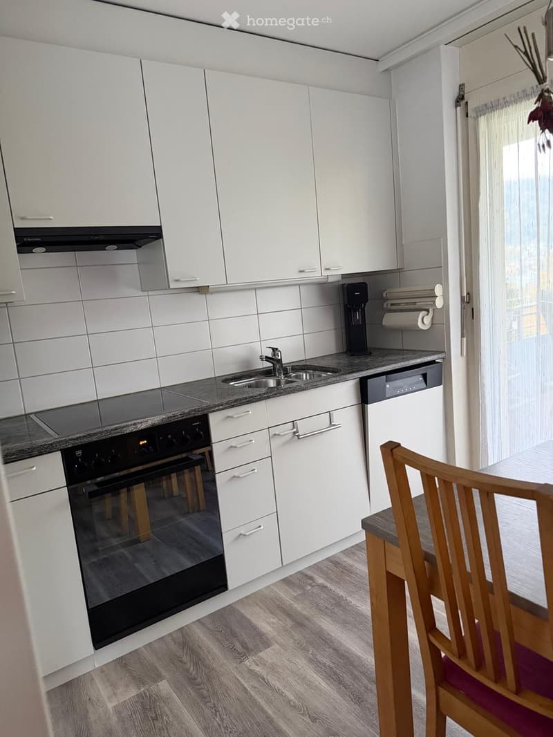 Modern kitchen with white cabinets, stainless steel appliances, granite countertops, and a wooden dining chair visible.
