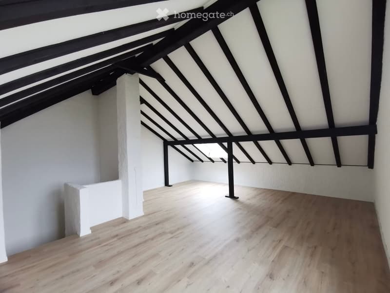 Empty attic space with wooden flooring, white walls, and exposed black wooden beams on the ceiling.