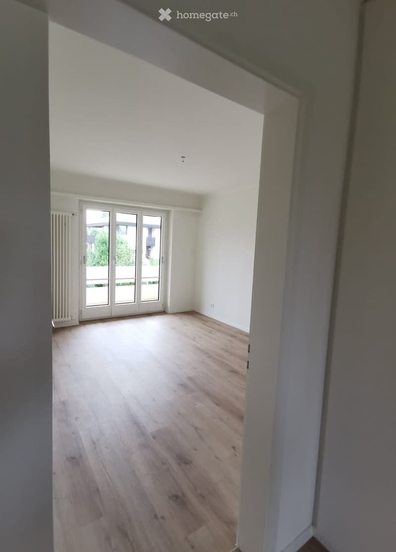 Empty room with wooden flooring, white walls, and large sliding glass doors leading to a balcony or outdoor area.