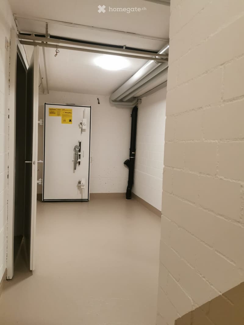 Empty hallway with white brick walls, concrete floor, and a white electrical panel with a yellow warning sticker on the left side.