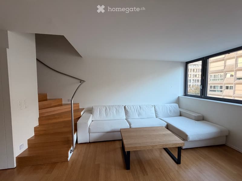 Modern living room with white walls, wooden flooring, a white sectional sofa, a wooden coffee table, and a tall floor lamp near the staircase.