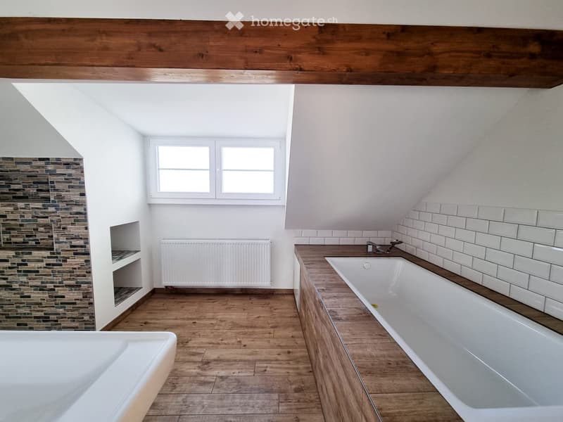 Bright attic bathroom with wooden floors, white tiled walls, two bathtubs, a window, and a radiator.