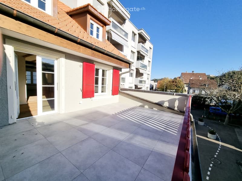 Balcony with tiled flooring, red railing, and view of neighboring buildings and parked cars.