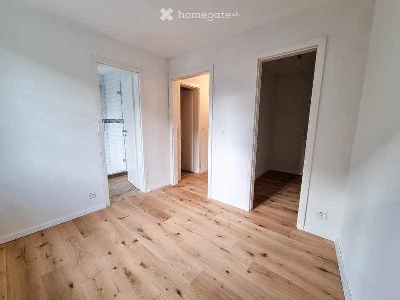 Empty room with light wooden flooring and white walls, featuring three open doorways leading to other spaces.