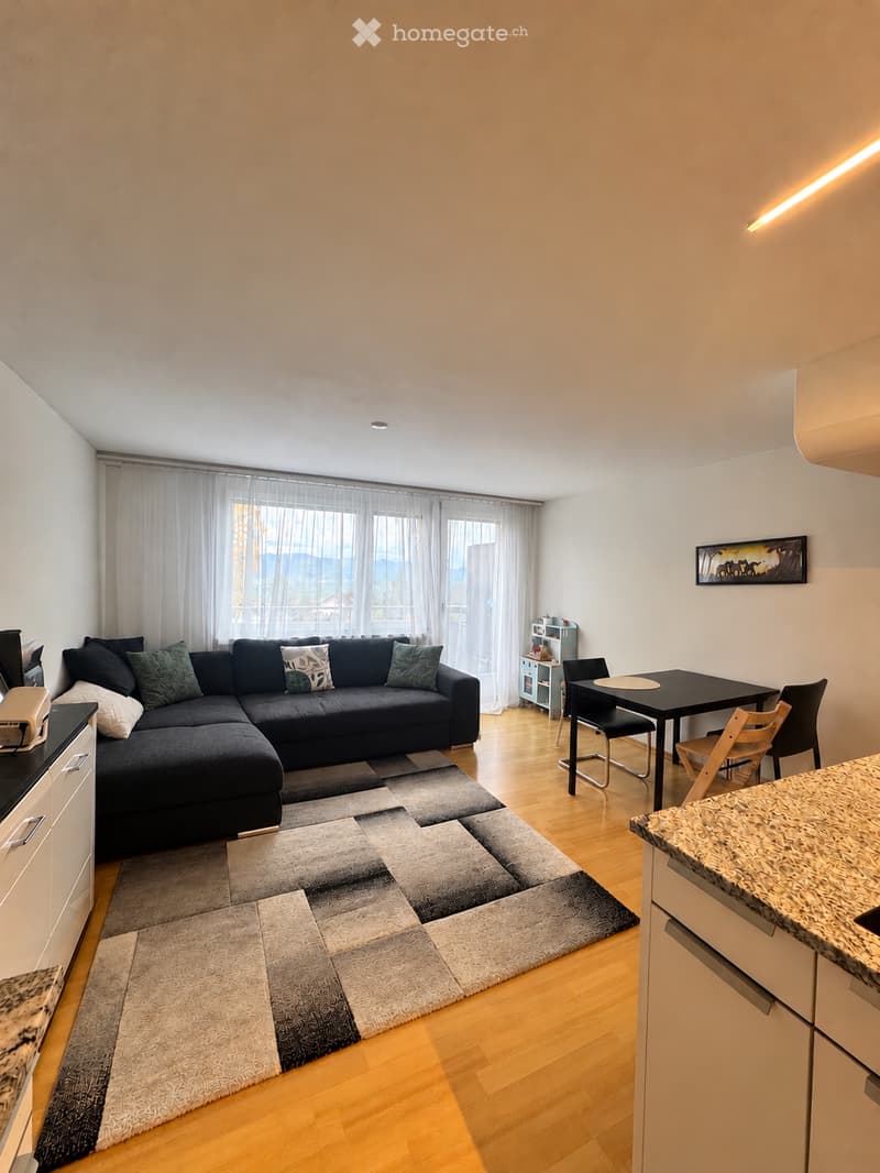 Modern living room with a sectional sofa, coffee table, dining area, and large windows with curtains.