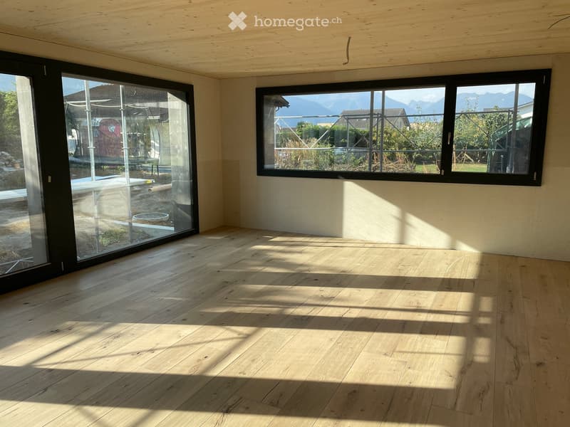 Empty room with wooden flooring, large windows, and a sliding glass door leading to an outdoor area.