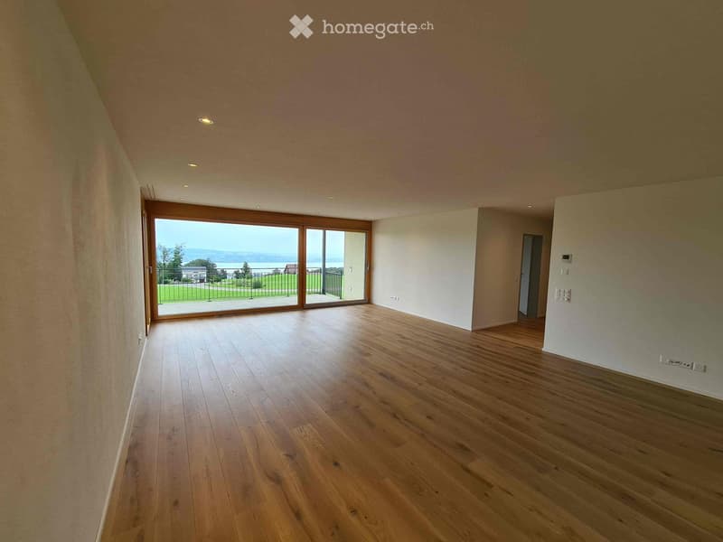 Empty room with wooden flooring, large sliding glass doors leading to a balcony with a scenic view, and recessed lighting.