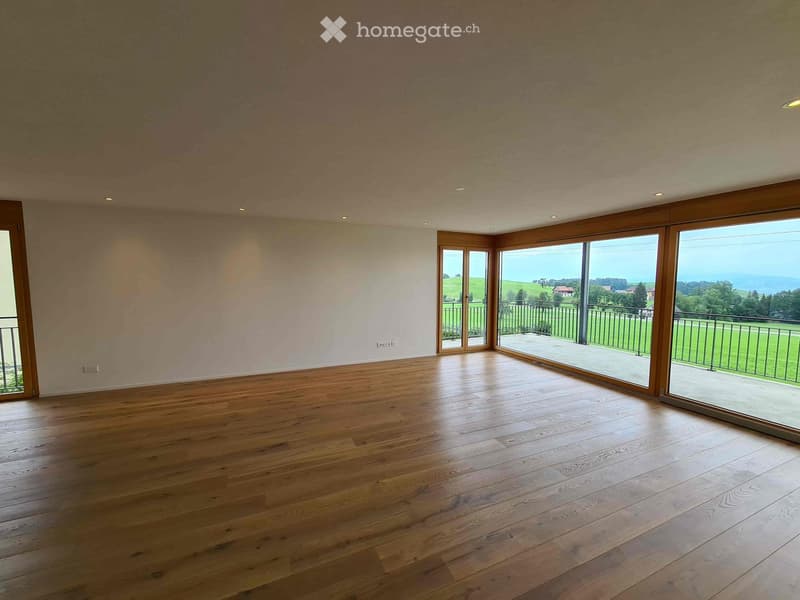 Empty room with wooden flooring, large windows, and a scenic view of the countryside and sea.