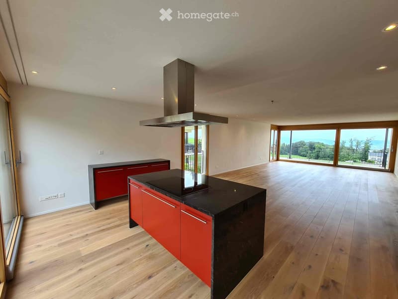 Modern kitchen with red cabinets, black island, and large windows overlooking the ocean.