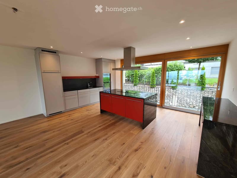 Modern kitchen with wooden flooring, stainless steel appliances, red and black cabinets, and a central island with a glass top.