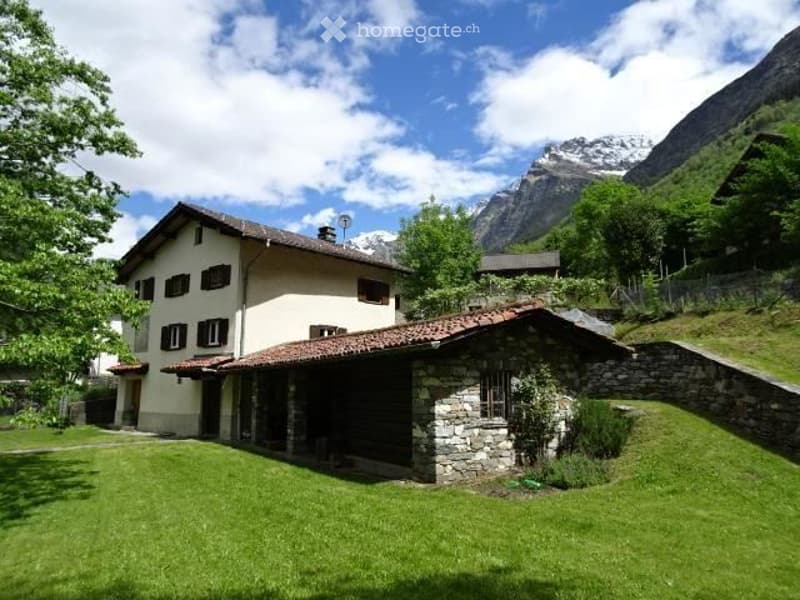 A two-story house with a stone garage and a well-maintained lawn, surrounded by trees and mountains.