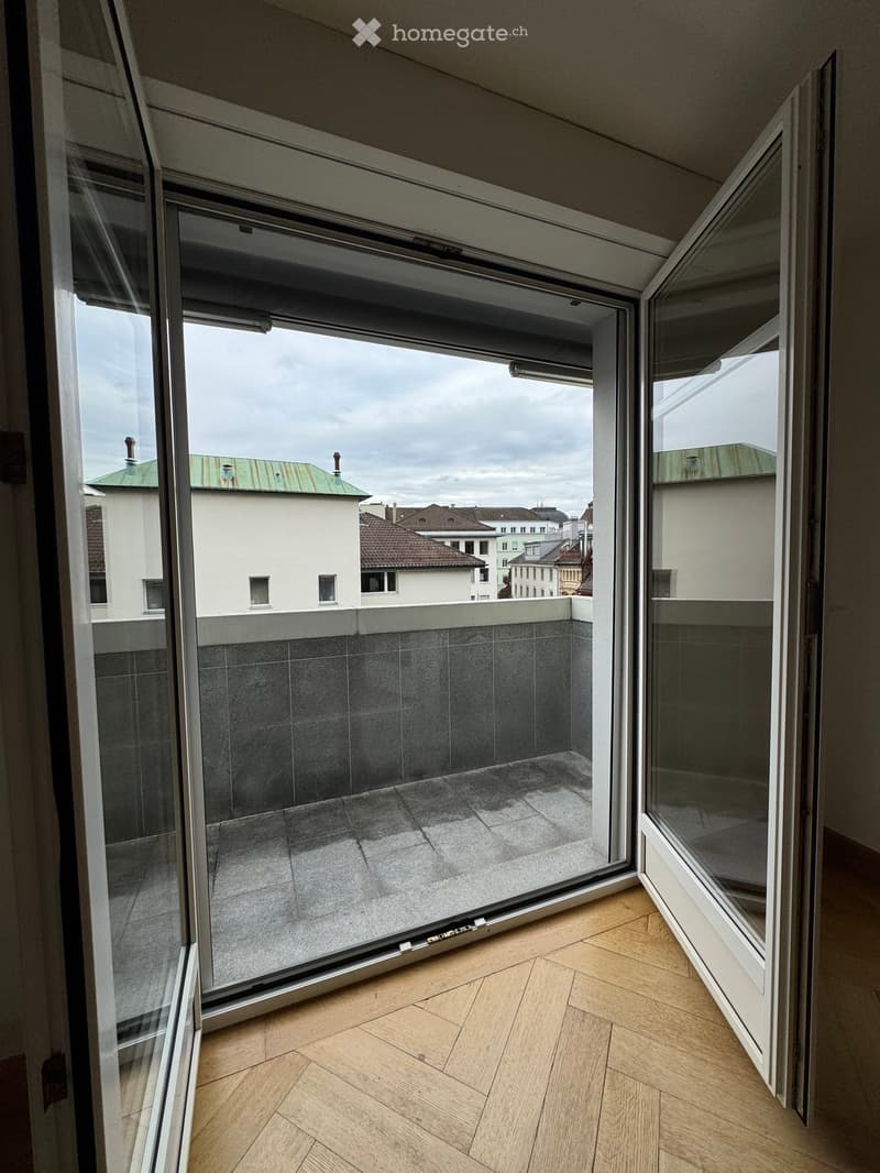 Open balcony with grey tiled floor, glass railing, and cityscape view.
