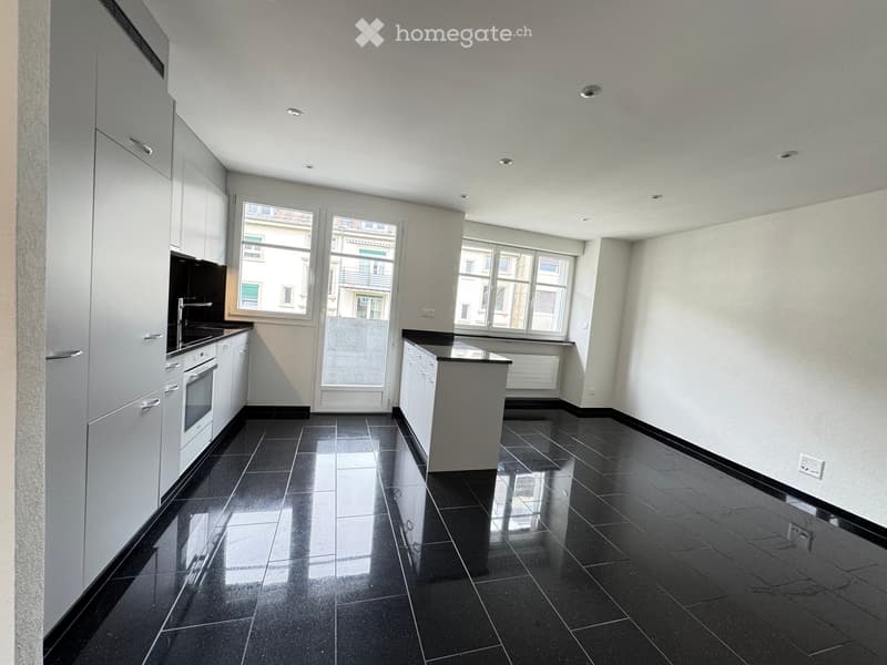 Modern kitchen with black tiled floor, white cabinets, and stainless steel appliances.