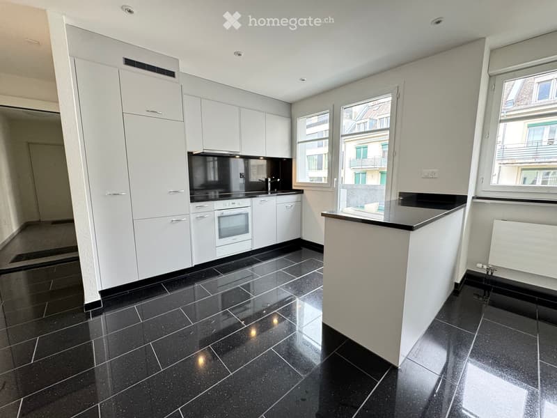 Modern kitchen with white cabinets, black countertops, and black tiled flooring. Features an oven, sink, and faucet.