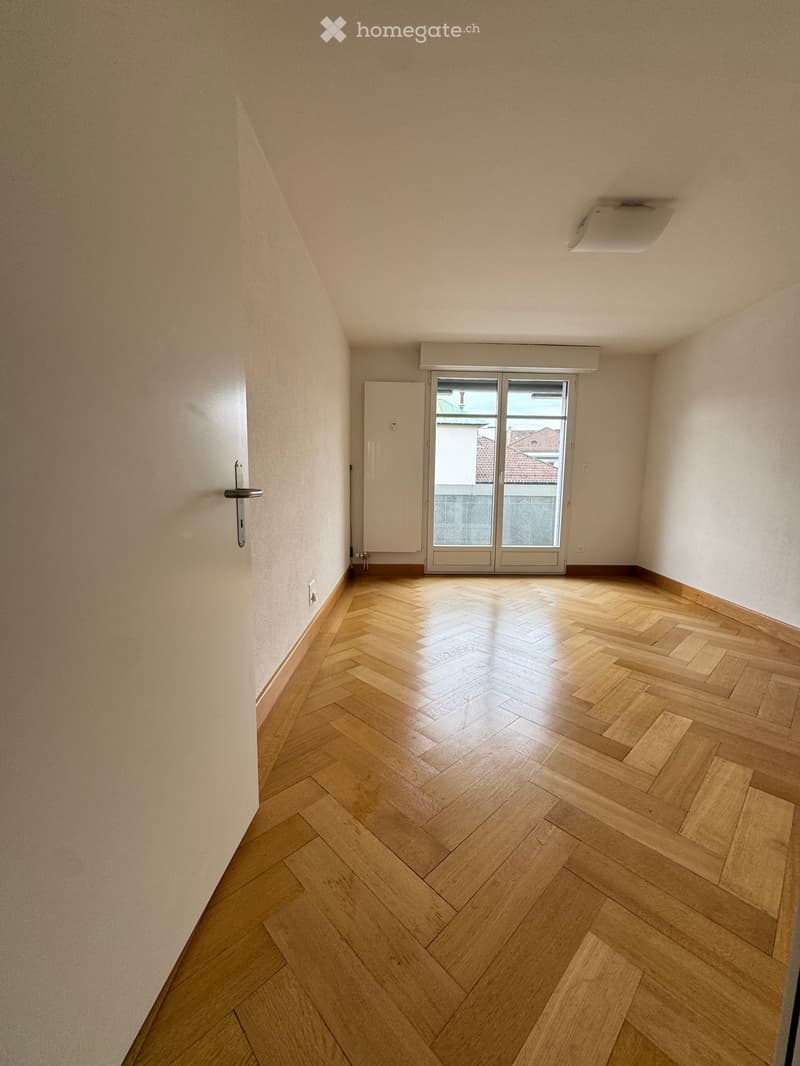 Empty room with wooden herringbone flooring, white walls, and a sliding glass door leading to a balcony.
